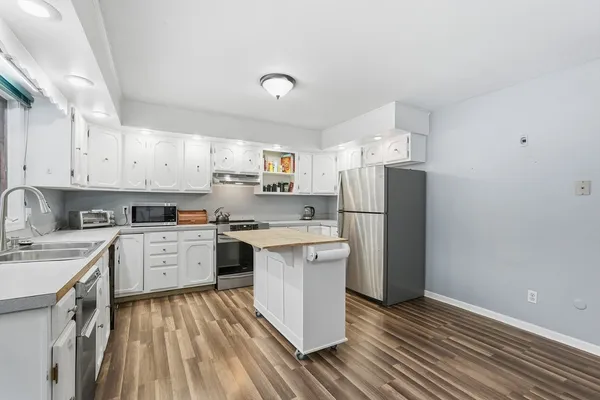 a kitchen with a sink dishwasher a refrigerator oven a sink dishwasher and white cabinets with wooden floor