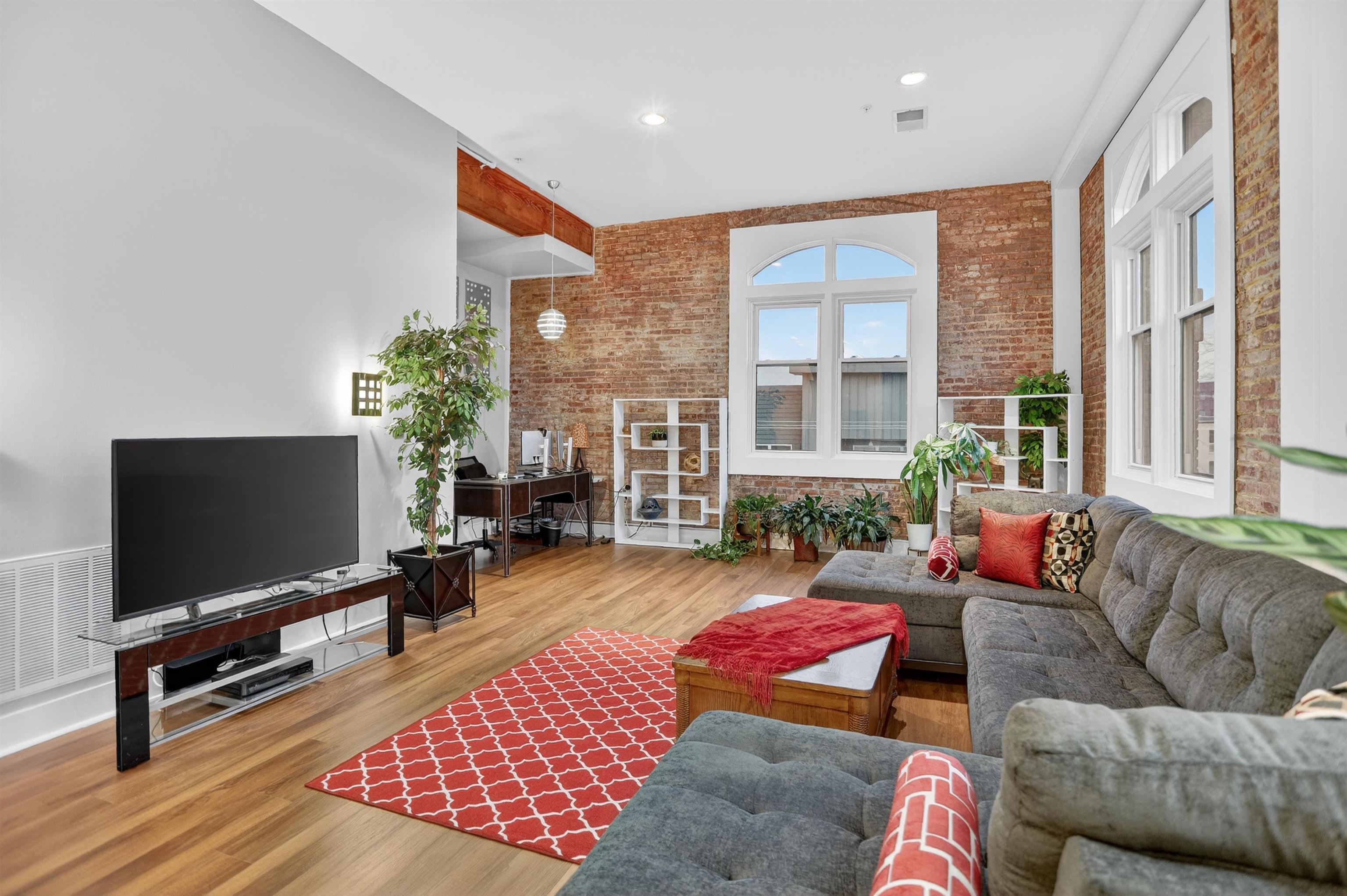 435 South Front Street, Unit 307 Memphis, TN 38103 - Photo 12 of 40 Living room featuring brick wall, wood finished floors, a towering ceiling, and recessed lighting