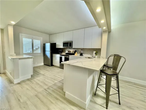 a kitchen with stainless steel appliances a stove a sink a refrigerator white cabinets and wooden floor