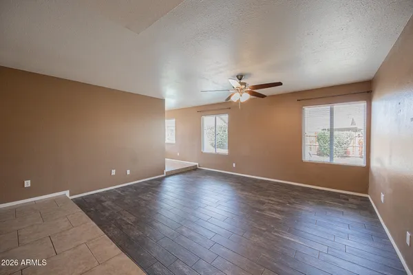 an empty room with wooden floor chandelier fan and windows