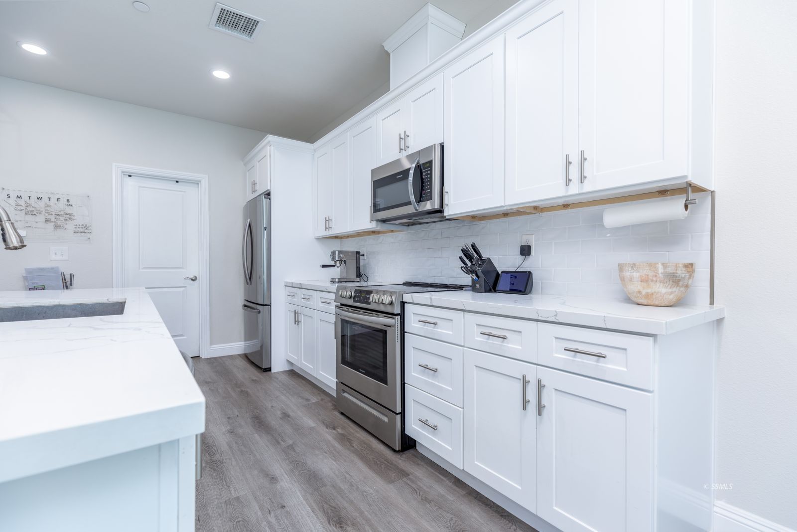 809 Paradise Drive Ridgecrest, CA 93555 - Photo 12 of 35 a kitchen with stainless steel appliances a sink dishwasher a refrigerator and white cabinets with wooden floor