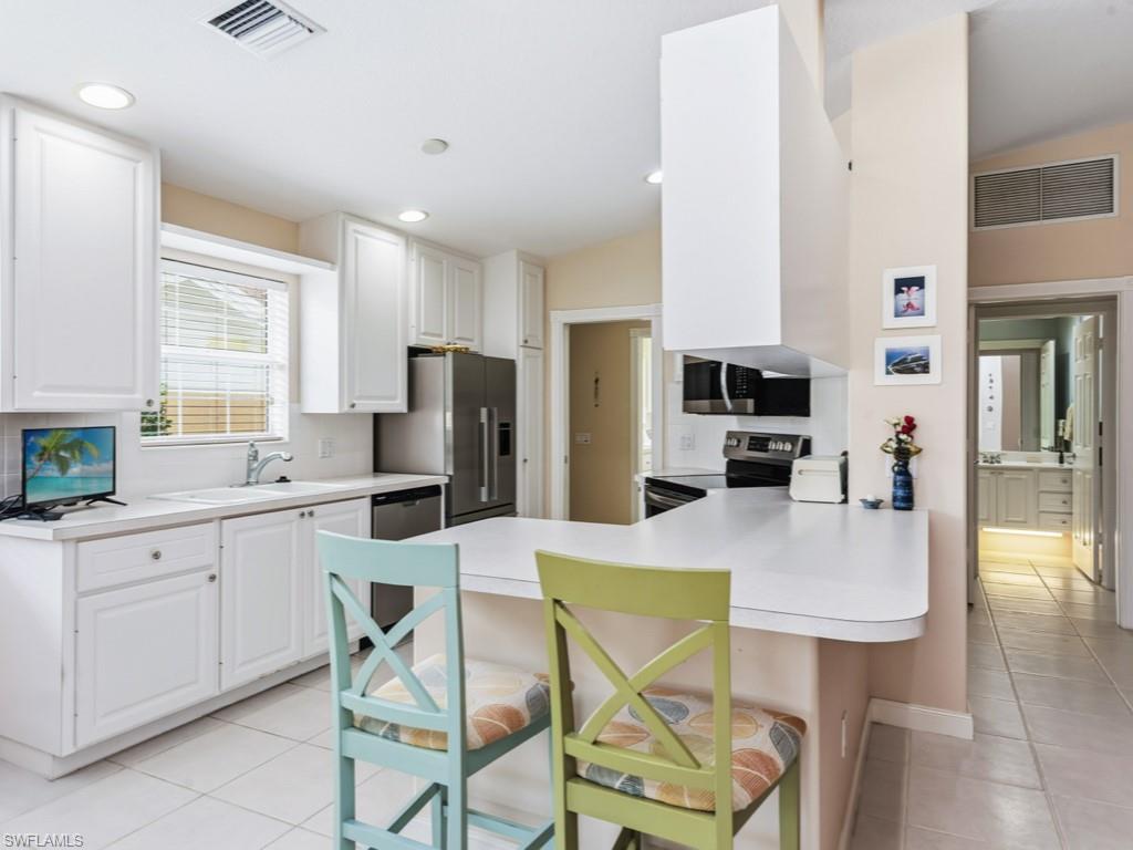 7520 Firenze Lane Naples, FL 34114 - Photo 9 of 32 a kitchen with stainless steel appliances kitchen island granite countertop a table chairs microwave and refrigerator