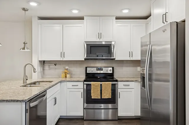 a kitchen with stainless steel appliances granite countertop a refrigerator a sink a stove and white cabinets