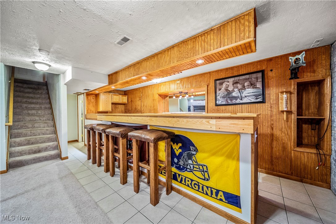 1951 Haines Road Madison, OH 44057 - Photo 29 of 44 Bar with a textured ceiling, wood walls, and light tile patterned floors