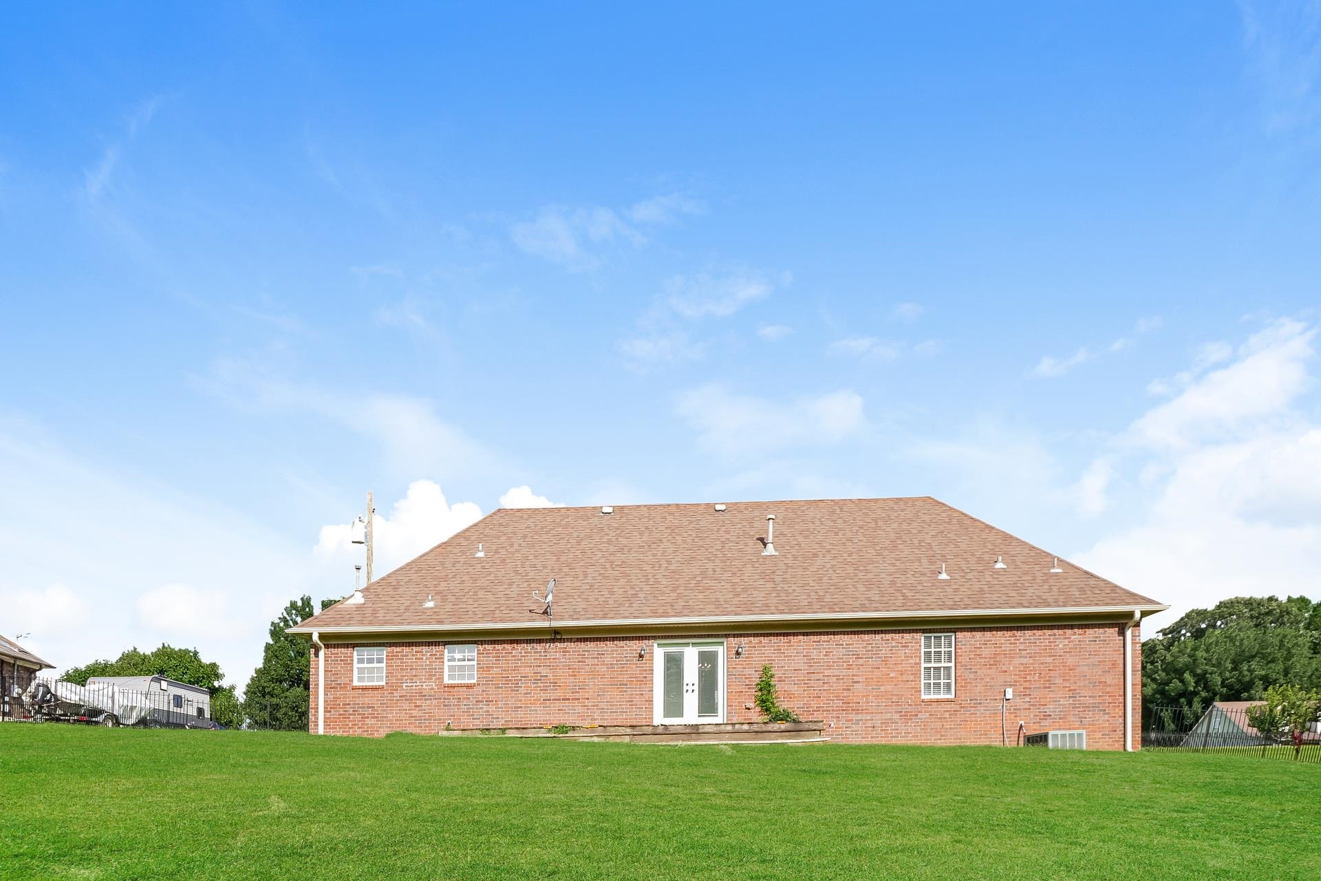 188 David Reed Drive Munford, TN 38058 - Photo 19 of 20 Expansive green lawn with a red brick exterior, featuring a brown shingle roof, white-framed double doors, and multiple windows