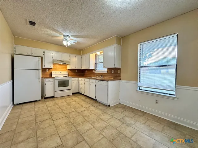 a kitchen with stainless steel appliances granite countertop a stove top oven a sink a refrigerator and white cabinets