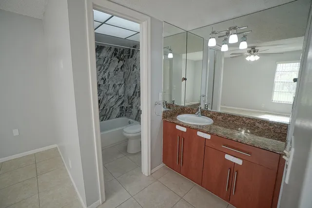 a bathroom with a granite countertop sink a toilet a mirror and shower