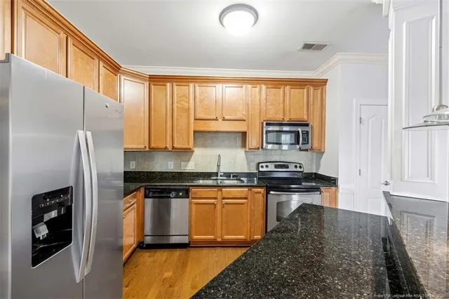 a kitchen with stainless steel appliances granite countertop a refrigerator a stove and a sink with wooden cabinets