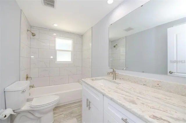 a bathroom with a granite countertop sink toilet mirror and bathtub