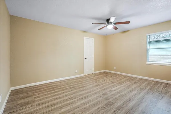 a view of an empty room with wooden floor and a ceiling fan
