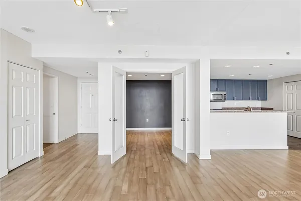 a view of an empty room and kitchen with wooden floor