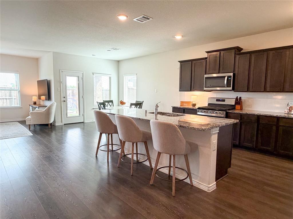 929 Philadelphia Street Fate, TX 75189 - Photo 34 of 34 a kitchen with stainless steel appliances granite countertop wooden floors a stove top oven a sink with island and chairs