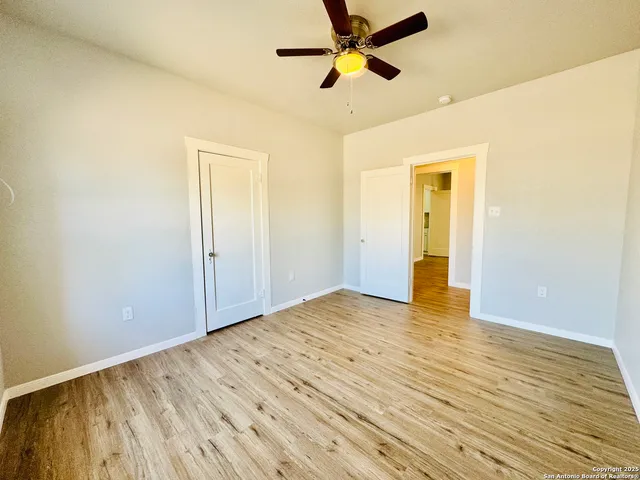 an empty room with wooden floor ceiling fan and windows