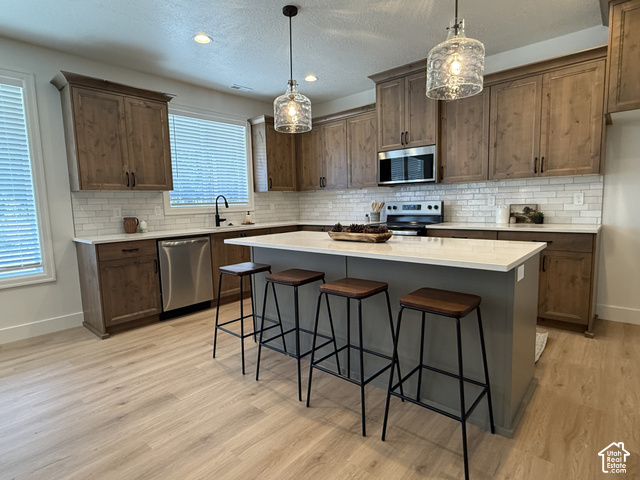 658 West 500 South, Unit 2 Logan, UT 84321 - Photo 2 of 18 Kitchen featuring wood-finish cabinetry, stainless steel appliances, a white subway tile backsplash, light-colored countertops, and pendant lighting