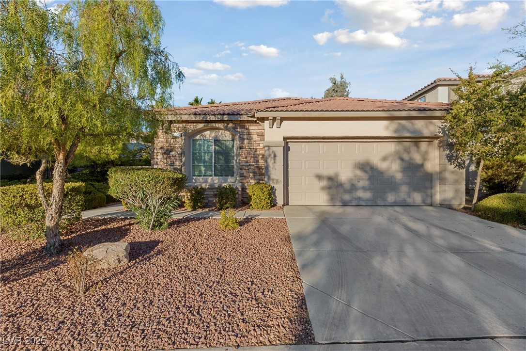 View of front facade with stone siding, driveway, an attached garage, stucco siding, and a tiled roof