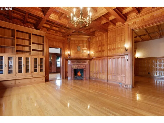 a view of an empty room with wooden floor fire place and windows