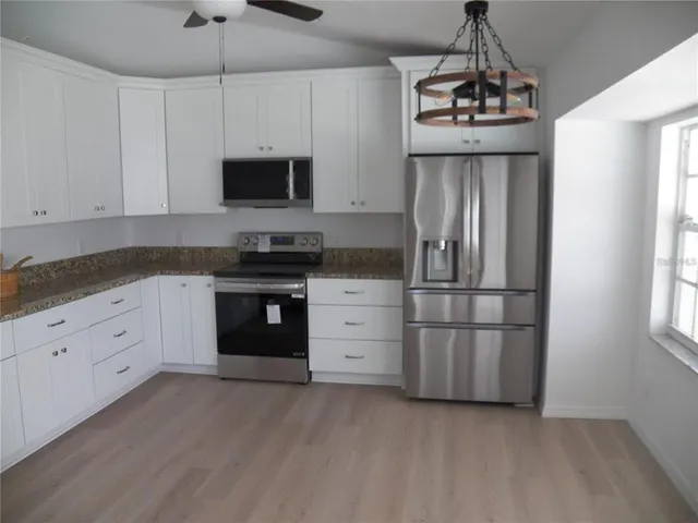 a kitchen with stainless steel appliances granite countertop a refrigerator a stove a sink and white cabinets