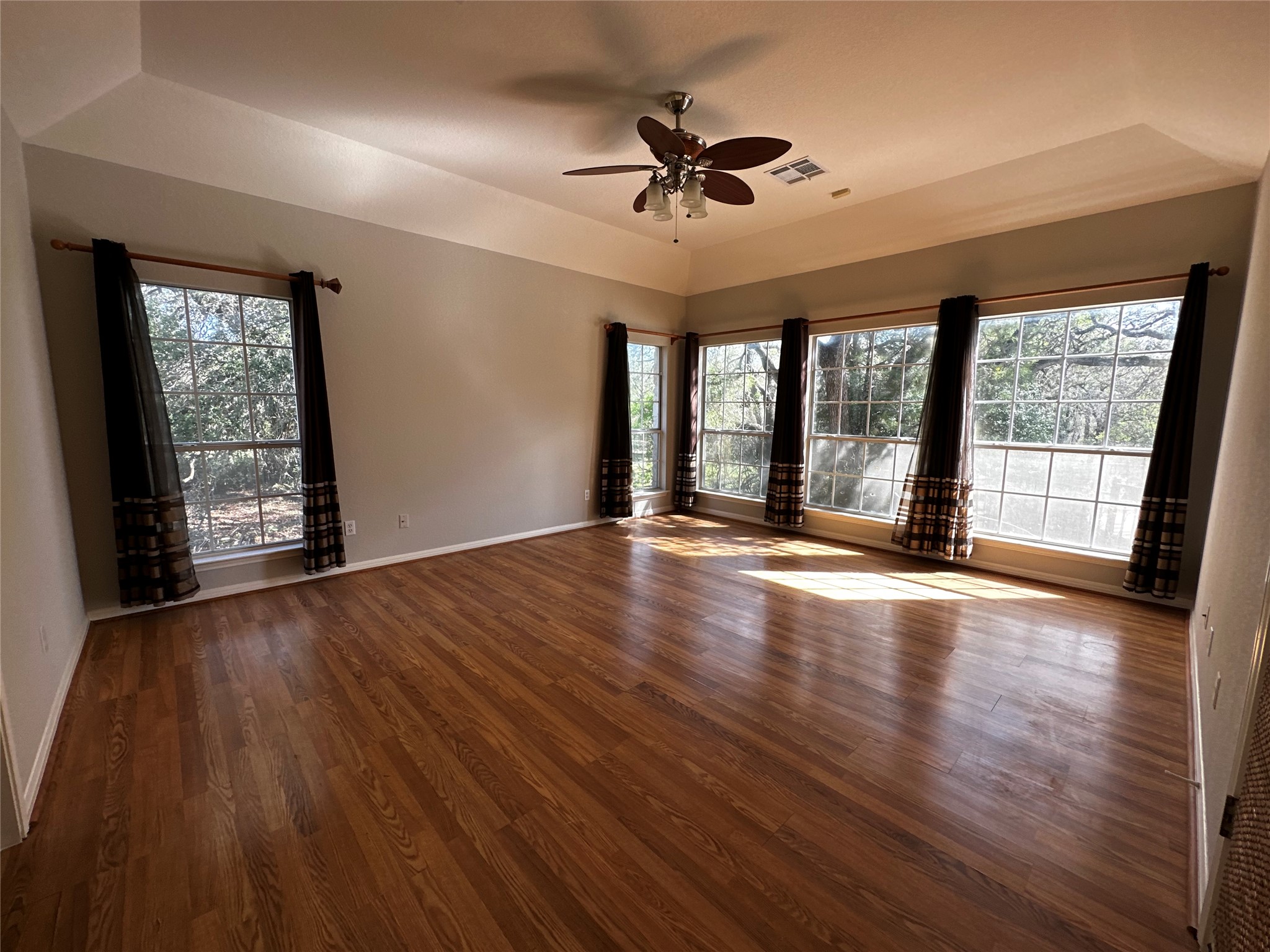 13615 Copperleaf Trail Manchaca, TX 78652 - Photo 15 of 39 Empty room featuring a tray ceiling, a ceiling fan, dark wood-style flooring, and plenty of natural light
