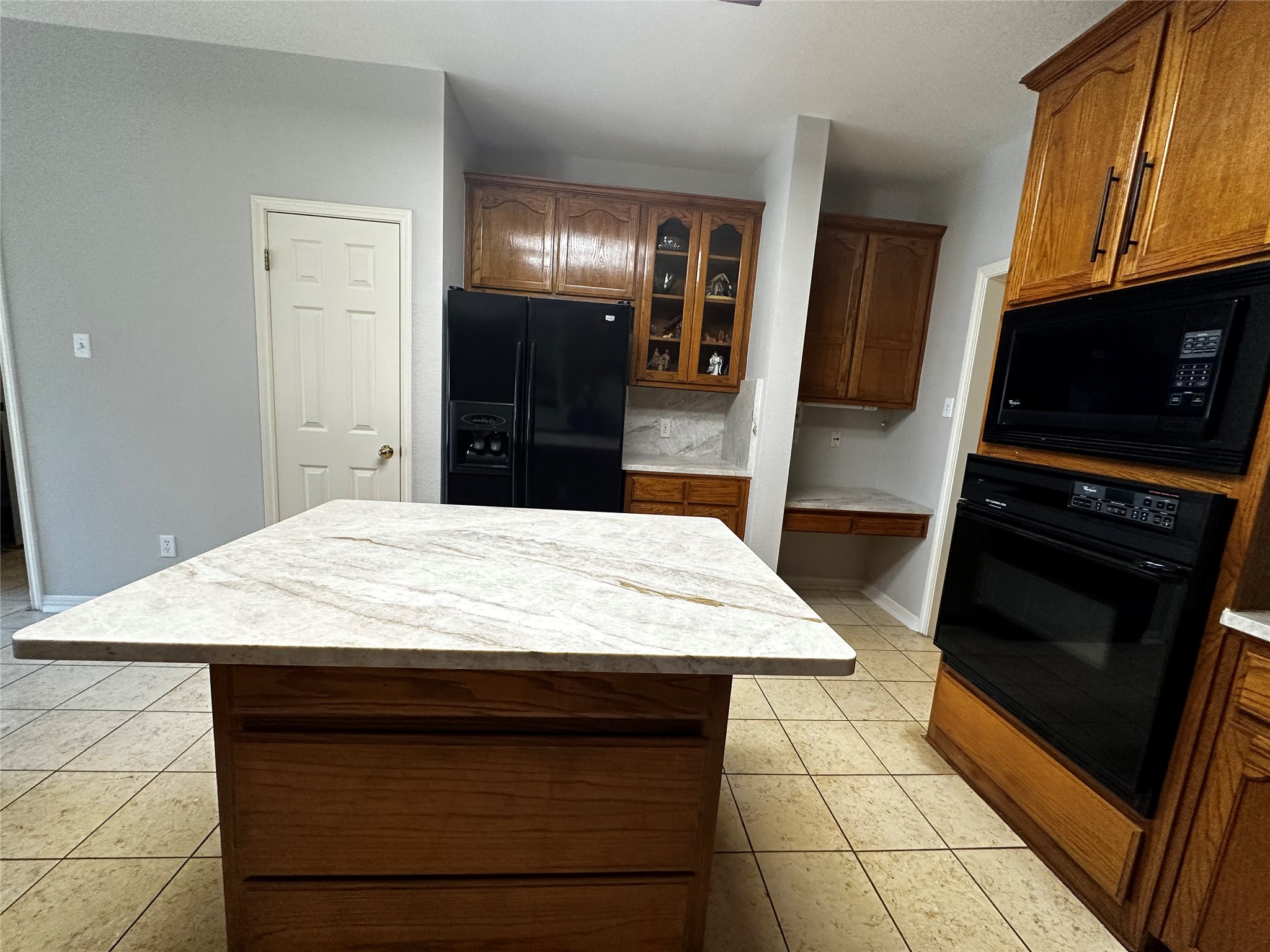 13615 Copperleaf Trail Manchaca, TX 78652 - Photo 16 of 39 Kitchen featuring glass fronted cabinets, black appliances, a center island, light tile patterned floors, and wood finish cabinetry