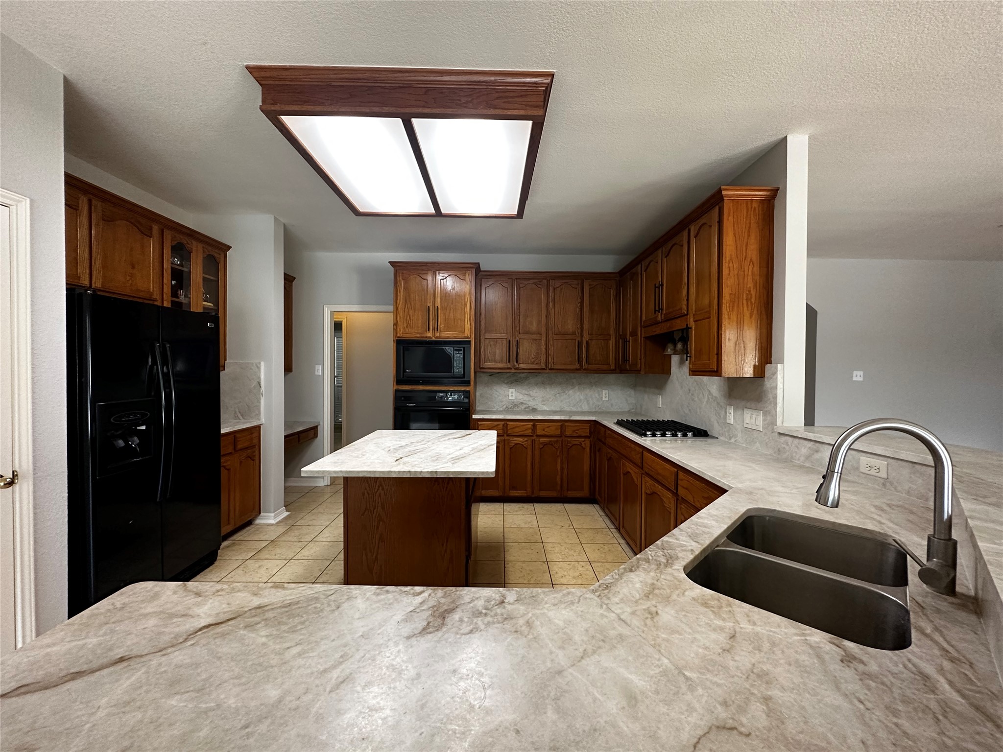 13615 Copperleaf Trail Manchaca, TX 78652 - Photo 18 of 39 Kitchen featuring black appliances, a kitchen island, glass fronted cabinets, light tile patterned floors, and tasteful backsplash