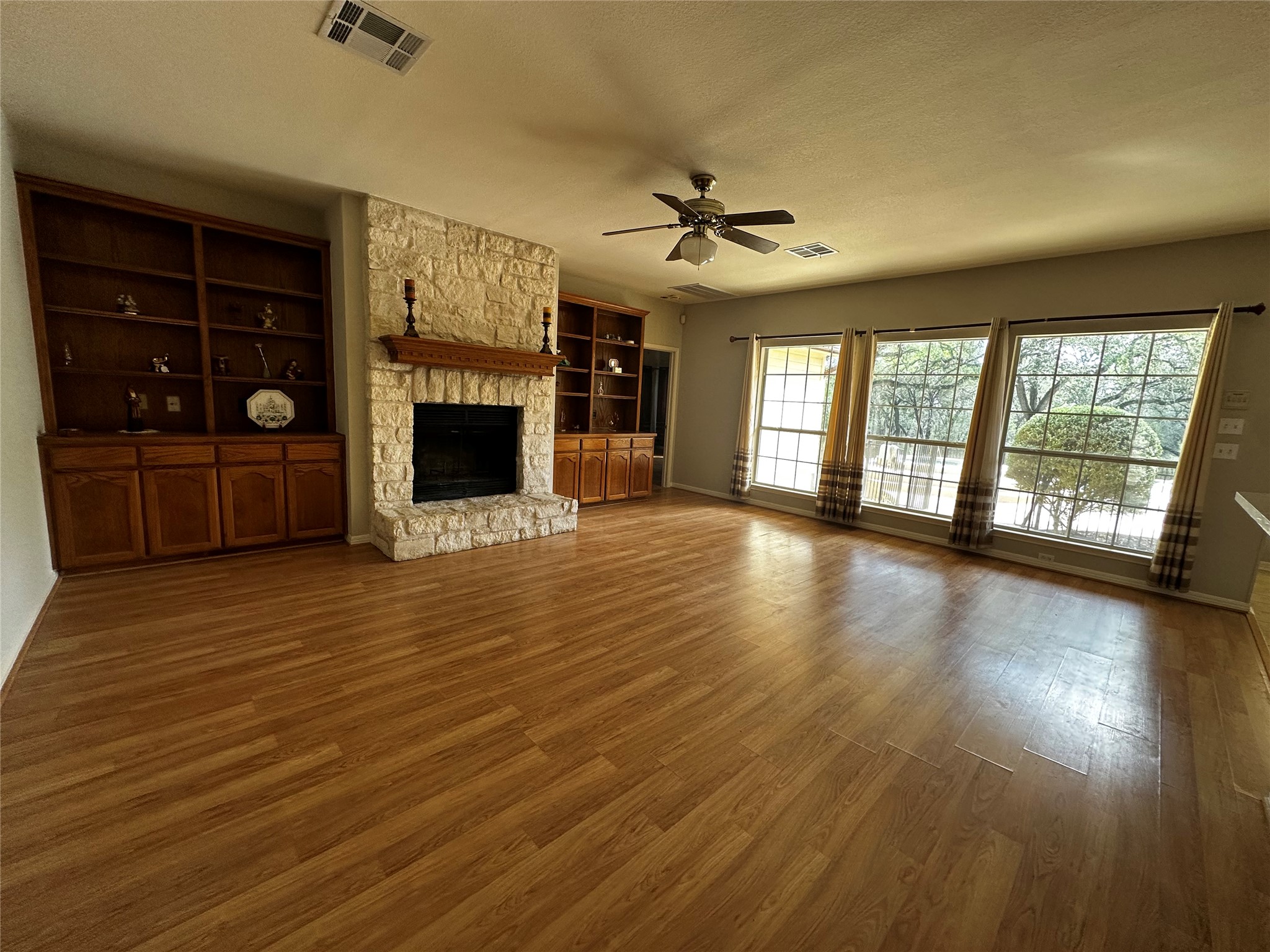 13615 Copperleaf Trail Manchaca, TX 78652 - Photo 10 of 39 Unfurnished living room featuring a fireplace, a textured ceiling, wood finished floors, a ceiling fan, and built in features