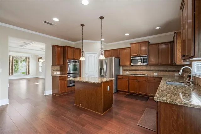a kitchen with kitchen island granite countertop wooden floors stainless steel appliances a sink a counter top space and cabinets