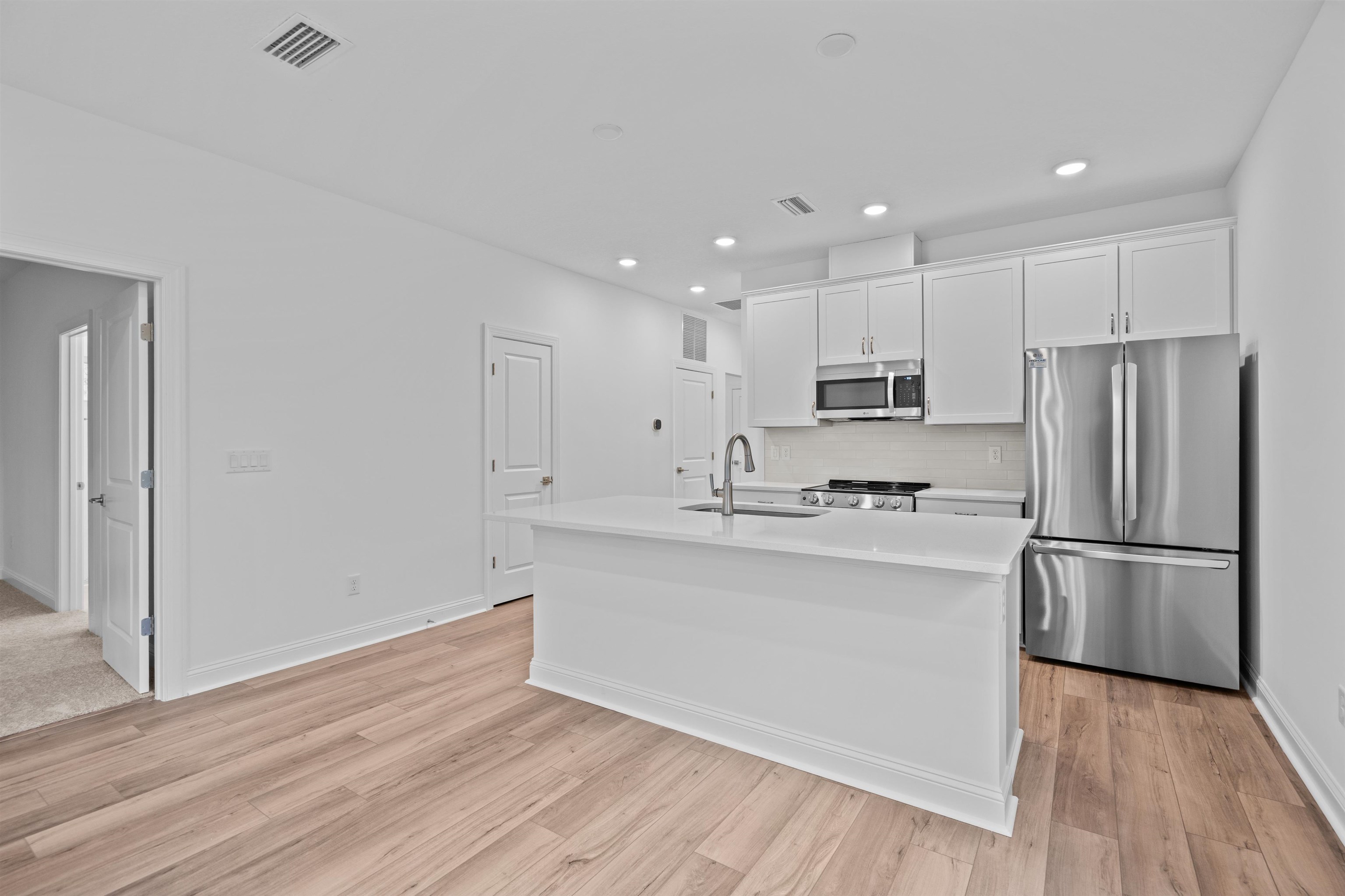 108 Aspen Road St. Augustine, FL 32086 - Photo 14 of 24 Kitchen featuring stainless steel appliances, white cabinetry, an island with sink, light wood-style flooring, and recessed lighting