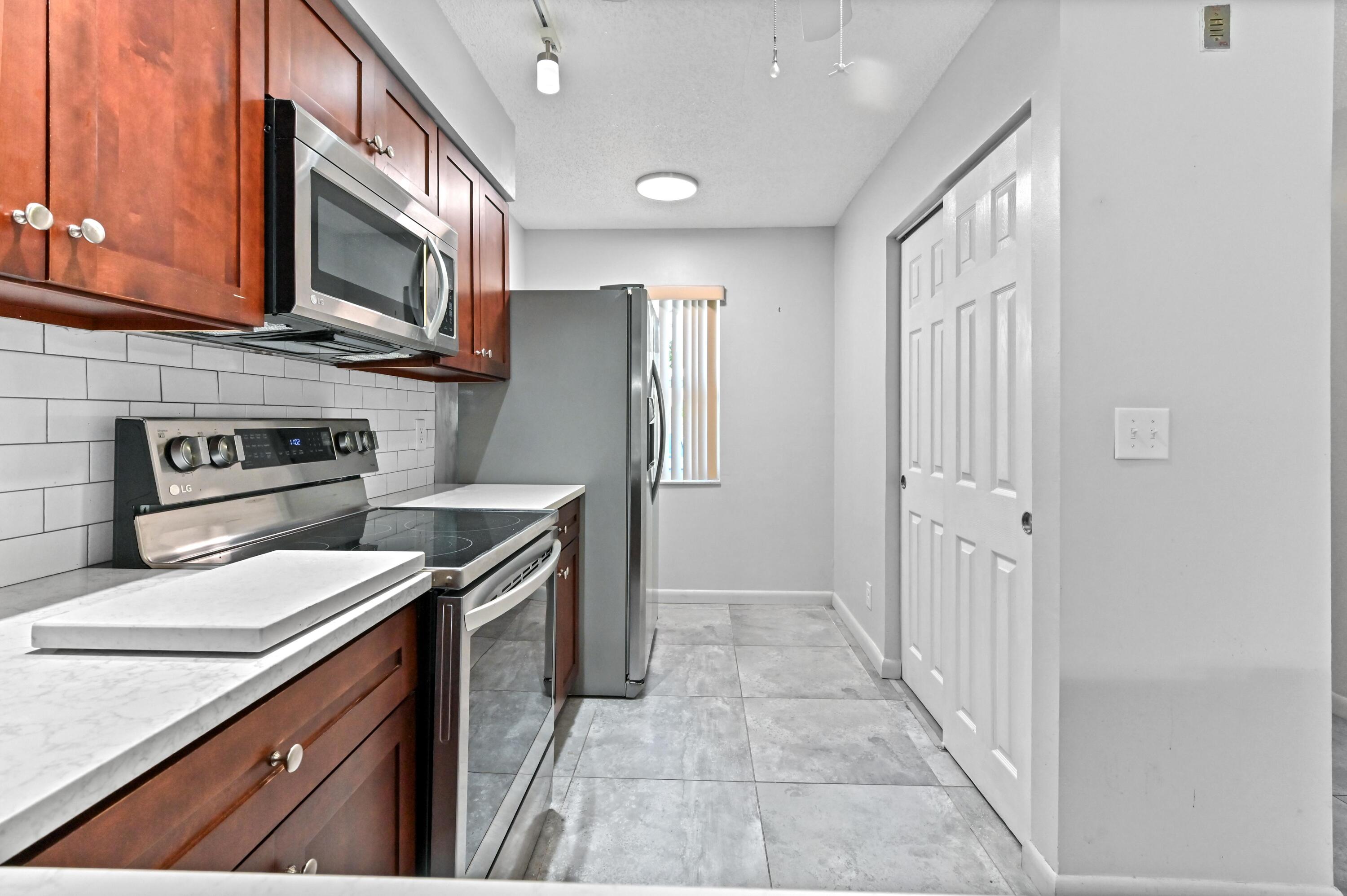 14895 Builtmore Way, Unit 107 Delray Beach, FL 33446 - Photo 11 of 40 a kitchen with stainless steel appliances granite countertop a refrigerator a stove and a sink with wooden cabinets