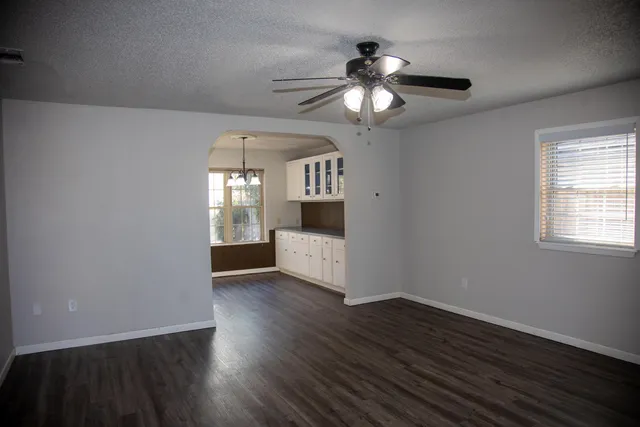 an empty room with wooden floor chandelier and windows