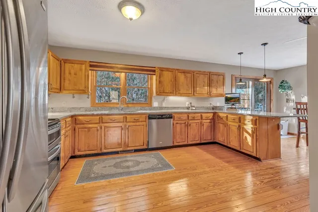 a kitchen with stainless steel appliances granite countertop a refrigerator a sink dishwasher a stove and white cabinets with wooden floor