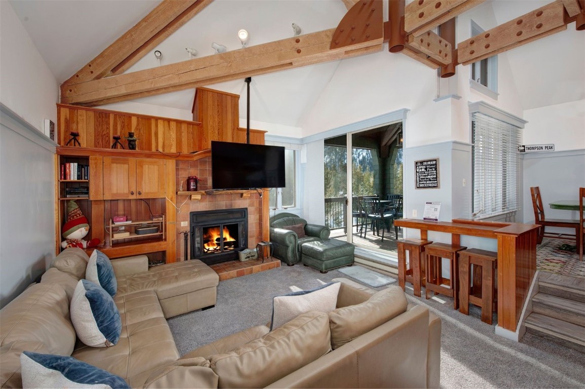 Living room featuring a fireplace, high vaulted ceiling, carpet, and beamed ceiling
