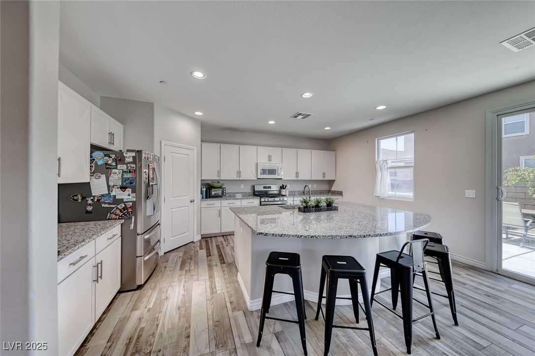 723 Gorringe Ridge Court Henderson, NV 89002 - Photo 13 of 48 Kitchen with light wood-style flooring, white cabinets, light stone counters, an island with sink, and recessed lighting