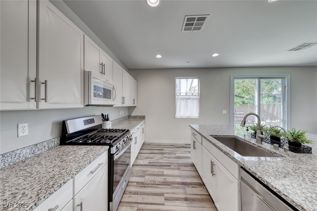723 Gorringe Ridge Court Henderson, NV 89002 - Photo 14 of 48 Kitchen with stainless steel appliances, white cabinetry, light wood-style floors, recessed lighting, and light stone countertops
