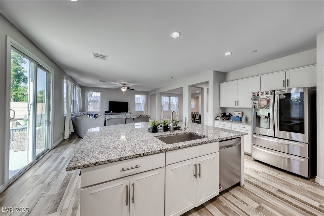 723 Gorringe Ridge Court Henderson, NV 89002 - Photo 15 of 48 Kitchen featuring appliances with stainless steel finishes, white cabinetry, light wood-style flooring, recessed lighting, and light stone counters