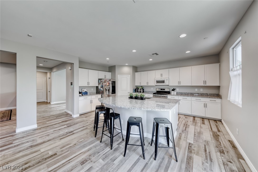 723 Gorringe Ridge Court Henderson, NV 89002 - Photo 16 of 48 Kitchen featuring white cabinetry, appliances with stainless steel finishes, light stone countertops, a kitchen island with sink, and recessed lighting