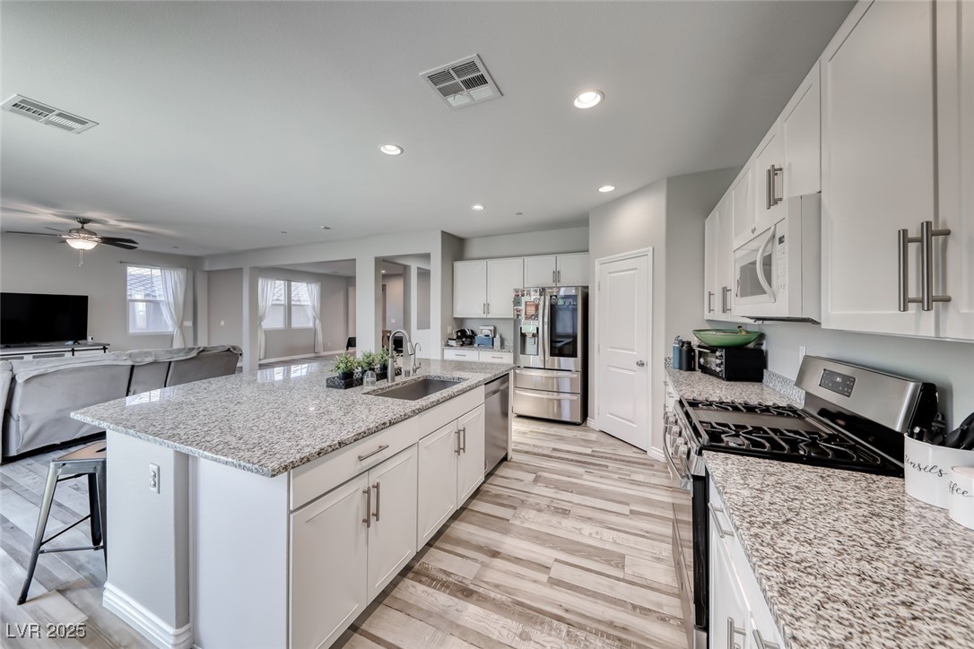 723 Gorringe Ridge Court Henderson, NV 89002 - Photo 17 of 48 Kitchen with appliances with stainless steel finishes, light wood finished floors, white cabinets, light stone countertops, and recessed lighting