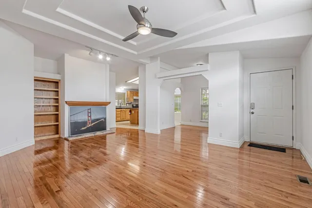 a view of a livingroom with a fireplace a ceiling fan and wooden floor