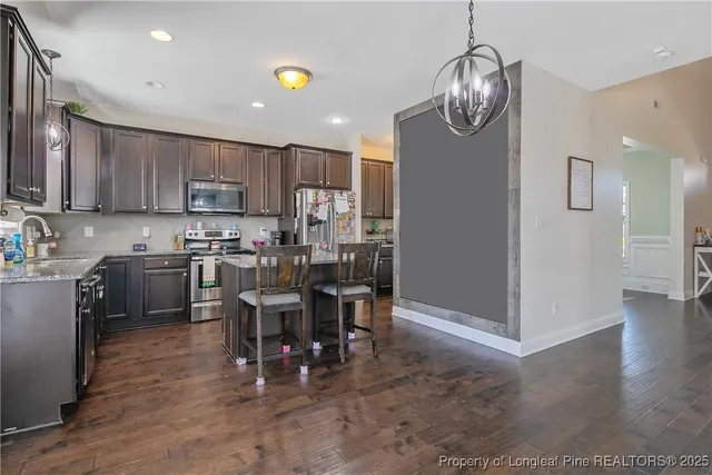 a open kitchen with stainless steel appliances granite countertop a stove top oven a sink dishwasher a dining table and chairs with wooden floor