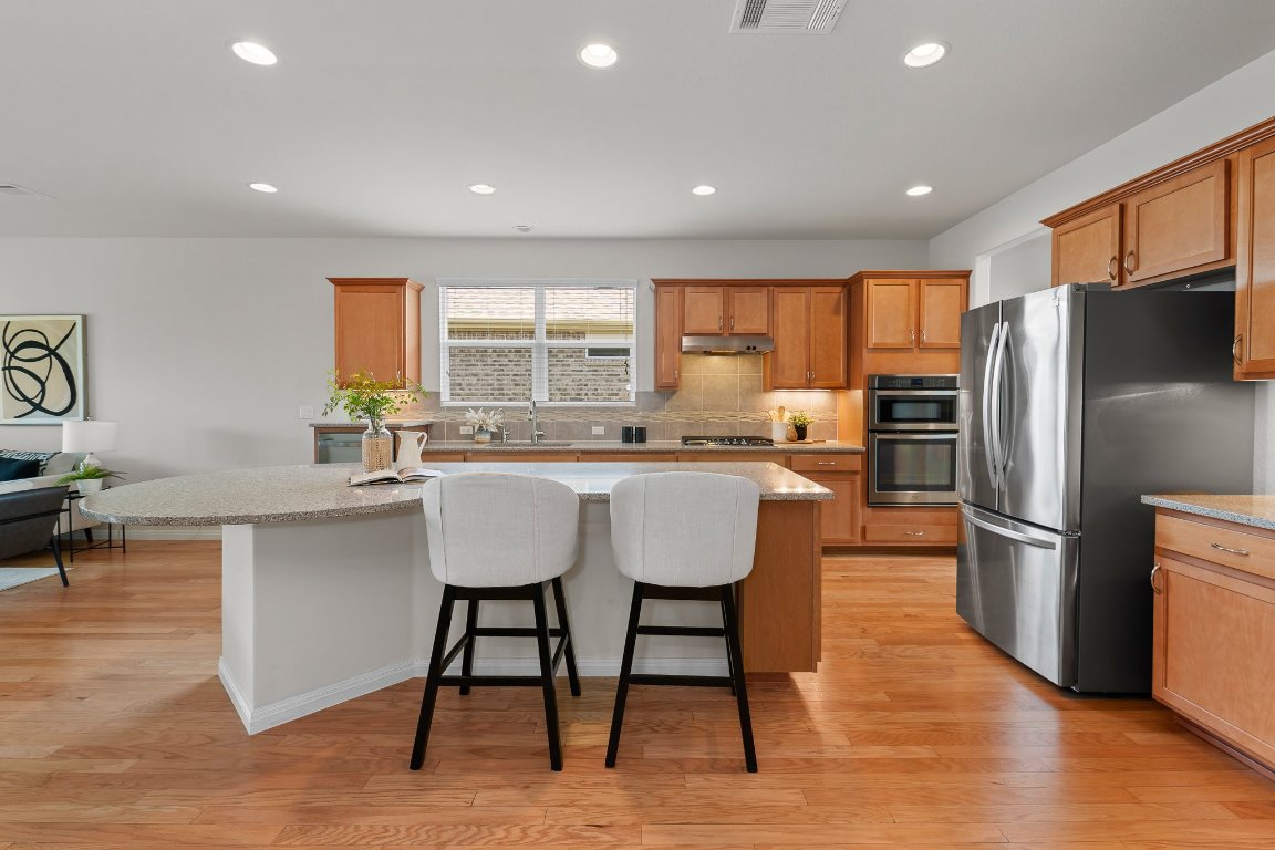 608 Kite Ridge Street Georgetown, TX 78633 - Photo 16 of 39 a kitchen with stainless steel appliances granite countertop a stove a sink a refrigerator and a refrigerator with wooden floor