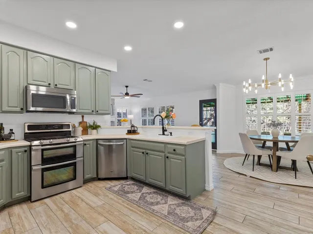 a kitchen with stainless steel appliances granite countertop a stove top oven a sink dishwasher a dining table and chairs with wooden floor