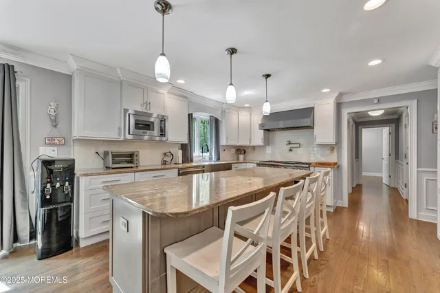 a kitchen with stainless steel appliances granite countertop a refrigerator a sink dishwasher a stove and white cabinets with wooden floor