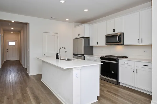 a kitchen with stainless steel appliances a stove top oven a sink a refrigerator white cabinets and wooden floor