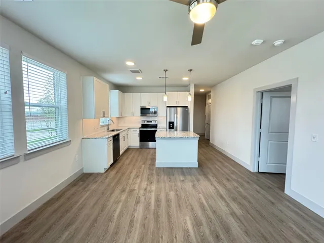 a large open kitchen with a refrigerator a stove top oven a sink dishwasher and white cabinets with wooden floor