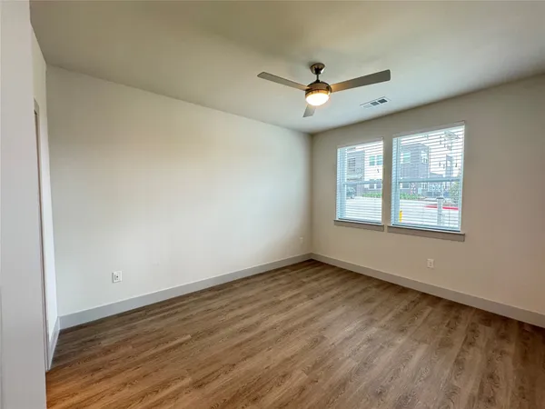 an empty room with wooden floor ceiling fan and windows