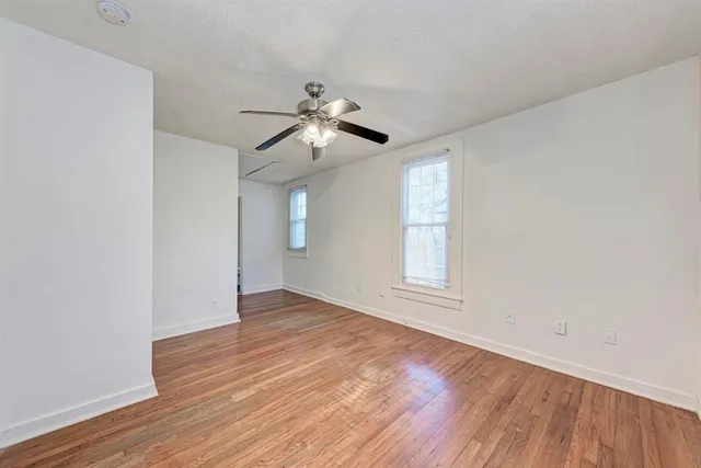 an empty room with wooden floor ceiling fan and window