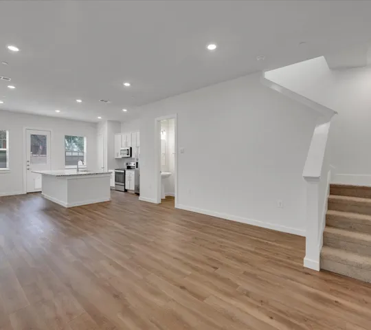 a view of empty room with wooden floor and kitchen
