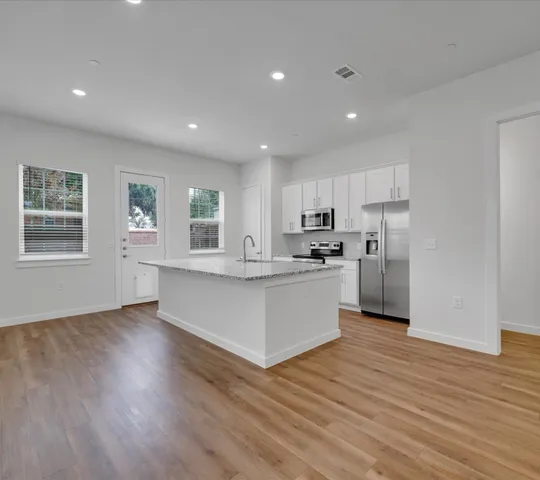 a large white kitchen with kitchen island a sink wooden floor and a refrigerator