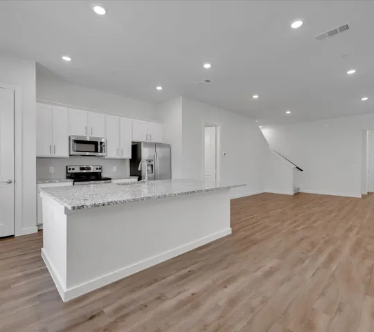 a large kitchen with stainless steel appliances granite countertop a stove a sink a refrigerator and white cabinets granite countertops with wooden floor