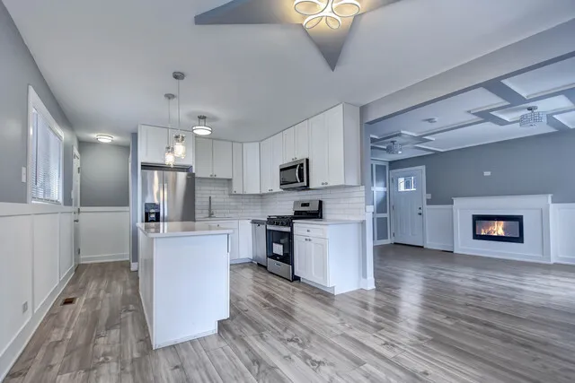 a kitchen with stainless steel appliances granite countertop a refrigerator a stove top oven a sink dishwasher and white cabinets with wooden floor