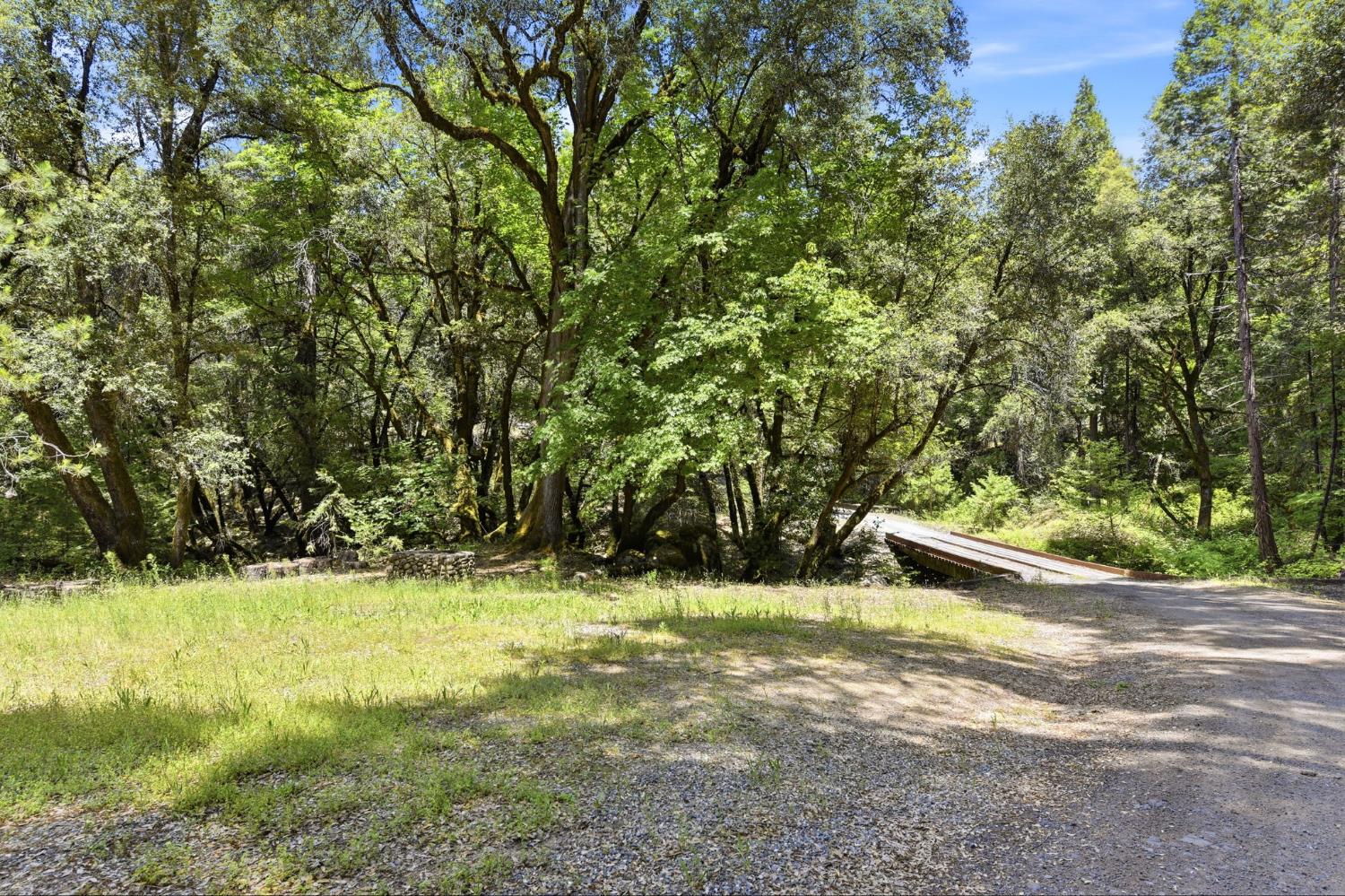 7201 Happy Valley Road Somerset, CA 95684 - Photo 67 of 75 Wooded property with a gravel road and grass area. There’s a little sitting area and picnic table to enjoy the sound of the year-round Butte Creek from this part of the property. The Road association took care of renovating the bridge over the creek last year.